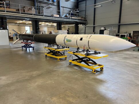 A slim white black and white rocket sitting horizontally in a warehouse